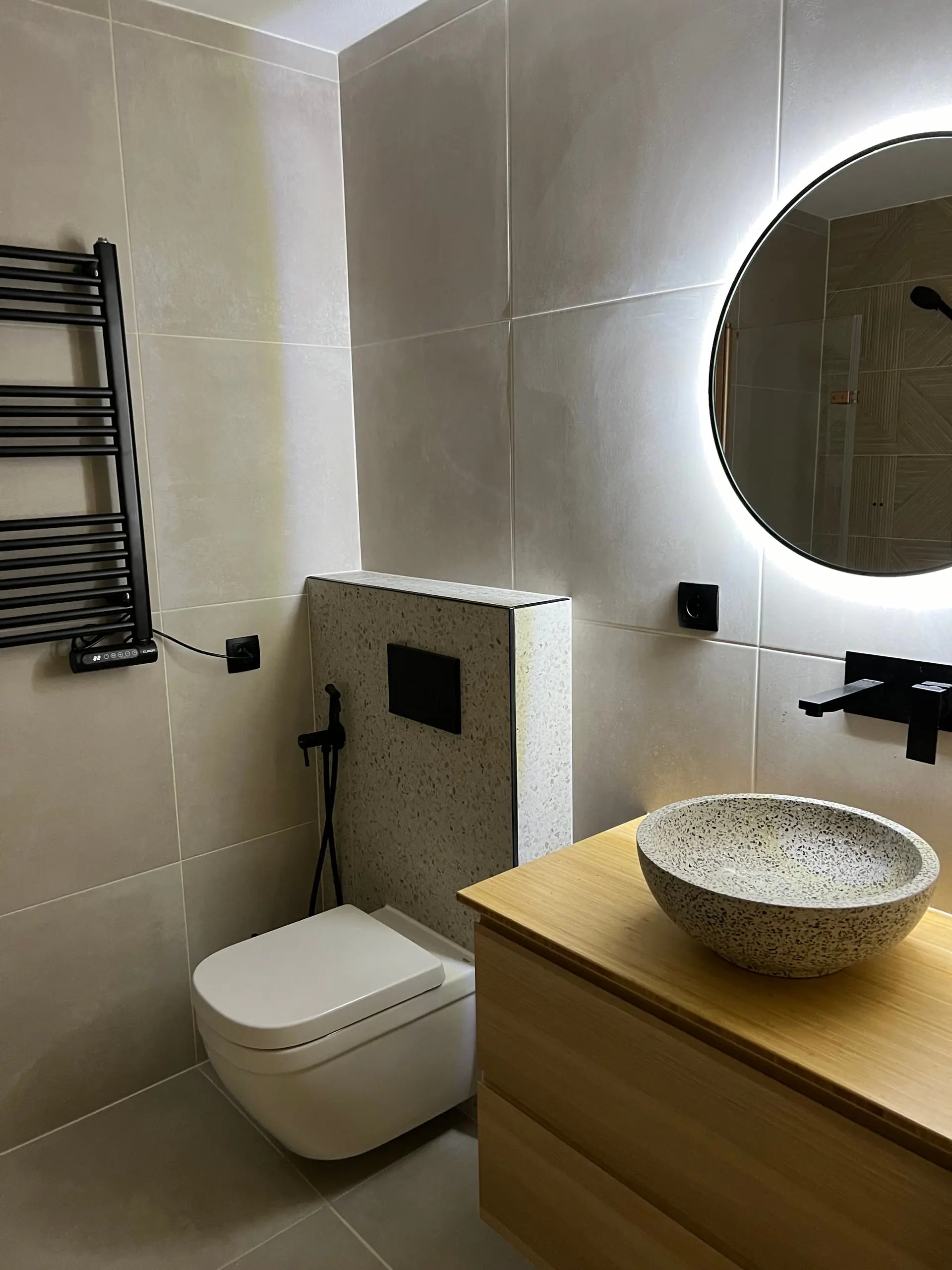 Badkamer met terrazzo waskom, bamboe meubel en verlichte spiegel in Geldrop